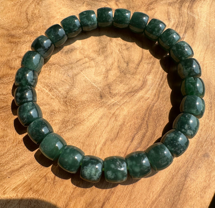A beaded stretch bracelet made of polished dark green stone beads with natural marbling, displayed on a warm brown wooden surface.