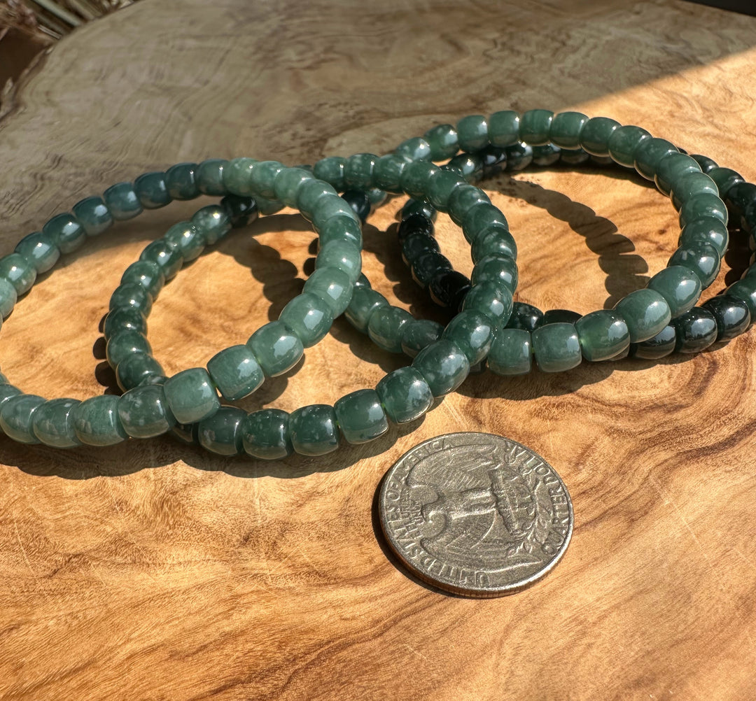 A set of green beaded stretch bracelets arranged on a wooden surface next to a US quarter for scale.