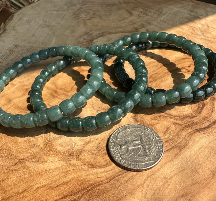 A set of green beaded stretch bracelets arranged on a wooden surface next to a US quarter for scale.