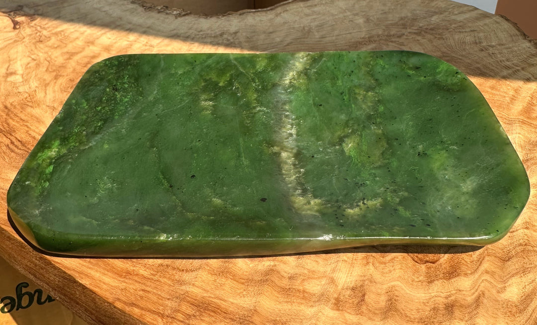 A polished green jade dish with rounded corners, resting on a natural wood slice background.