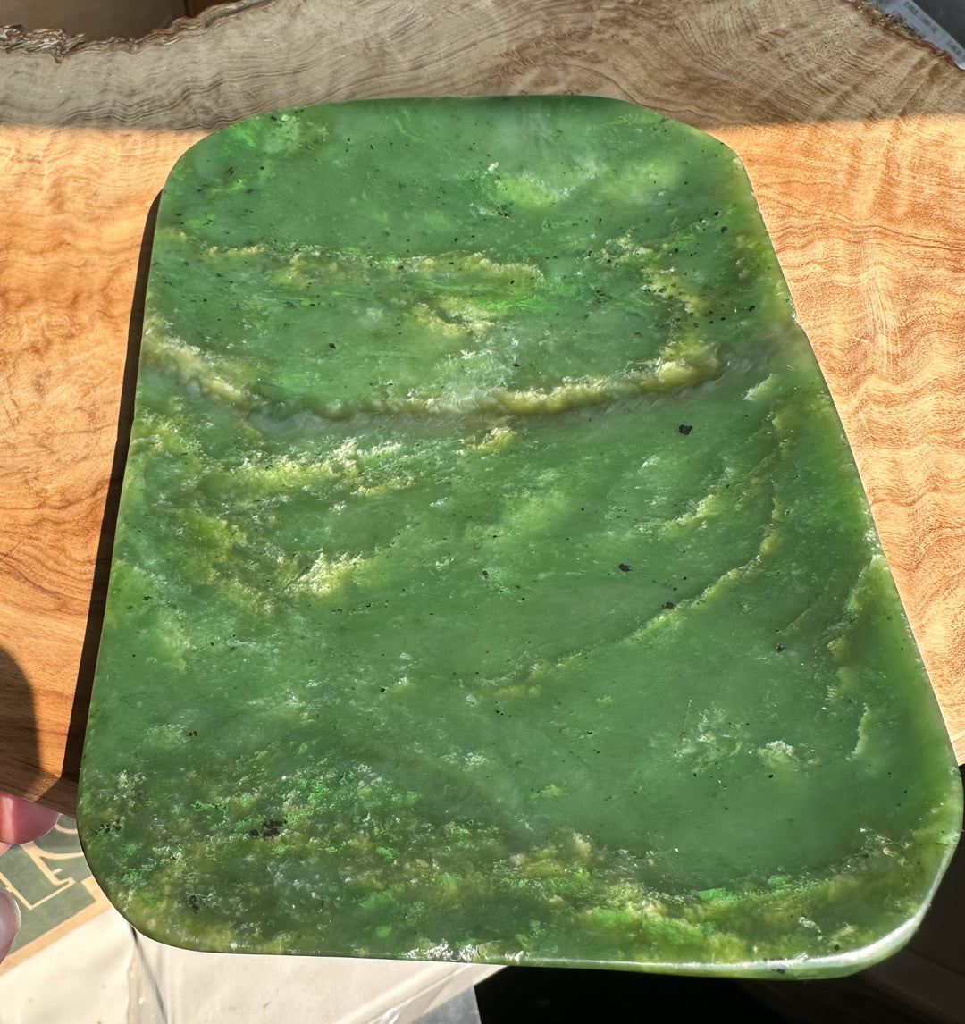 A rectangular green jade dish with rounded corners, showing natural marbled green and yellowish-green veining, photographed on a wood surface.