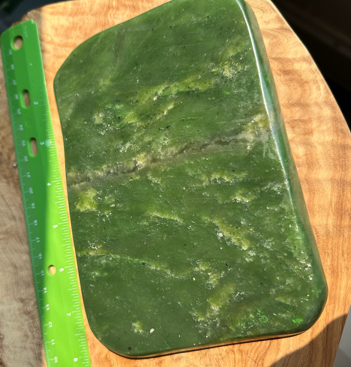 A polished green jade with rounded corners and a smooth glossy finish, shown next to a green ruler on a wooden cutting board.