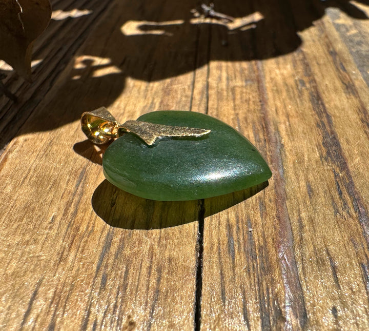 Green jade heart pendant with a gold bail on a wooden surface.