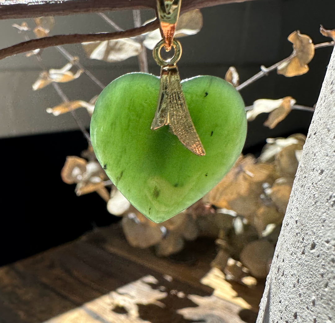 Green jade heart pendant with a gold bail suspended from a twig