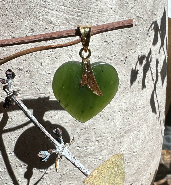 Green jade heart pendant with a gold bail against a light textured wall