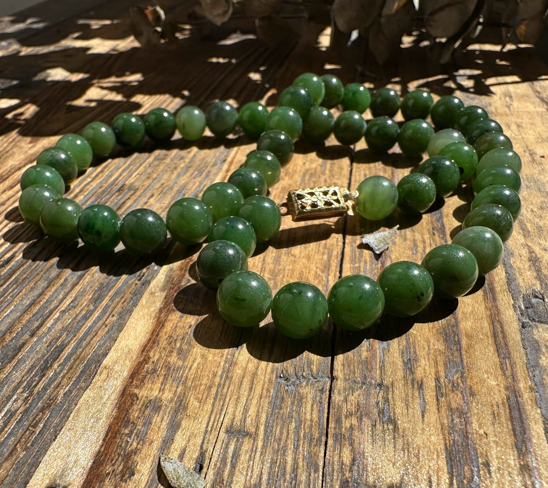 8mm Canadian nephrite jade beads necklace with a decorative gold clasp on wood.
