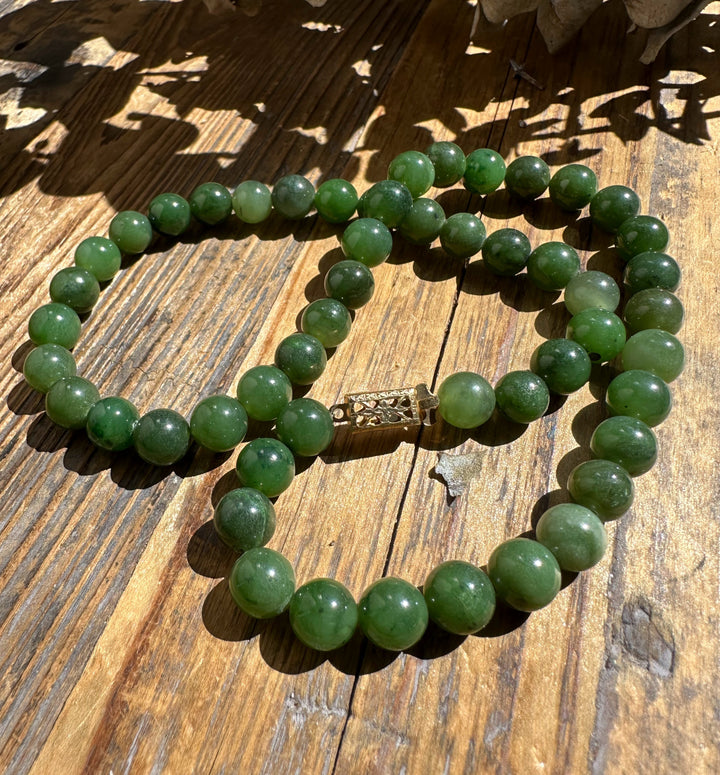 Nephrite jade bead necklace with an ornate clasp laid on sunlit wood