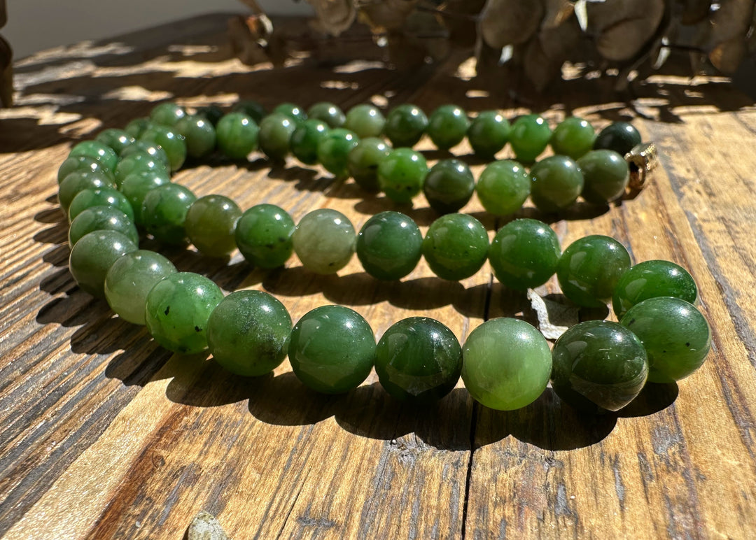 8mm Canadian nephrite jade bead necklace coiled on a sunlit wooden surface