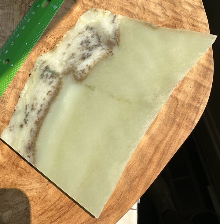 A translucent pale jade with a mottled brown and cream pattern along one edge, placed on a wooden surface next to a green ruler.