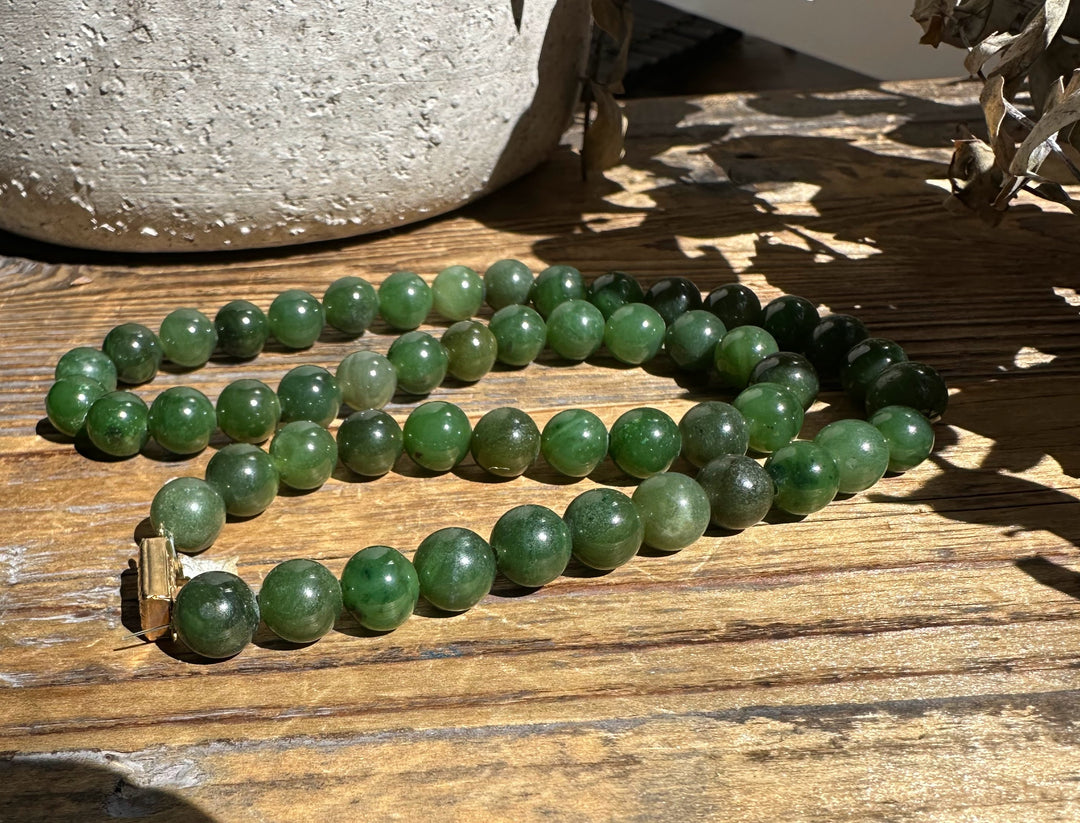 Green jade bead necklace with a gold tone clasp resting on a wooden surface