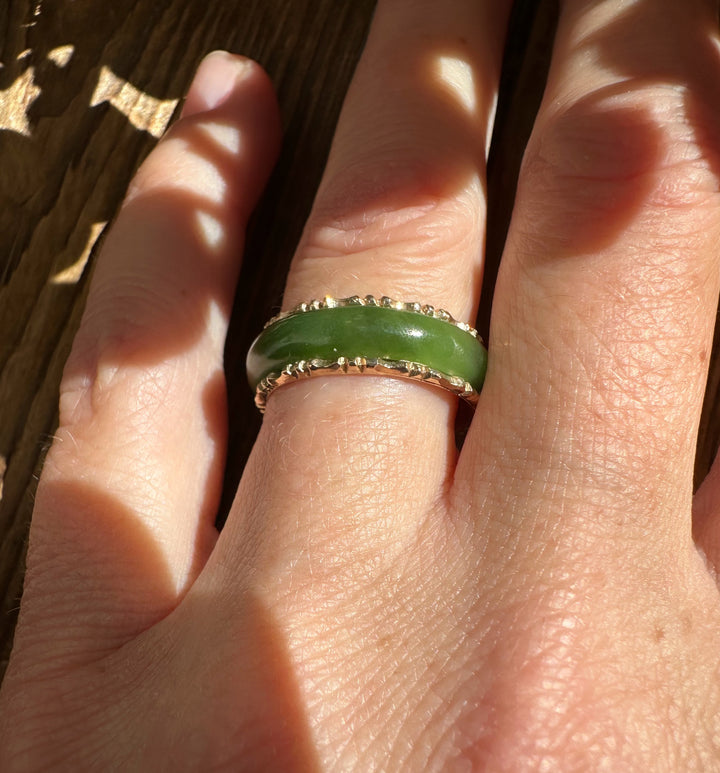 Close-up of the vintage jade ring on a finger, highlighting the green jade band and gold-toned decorative edge.
