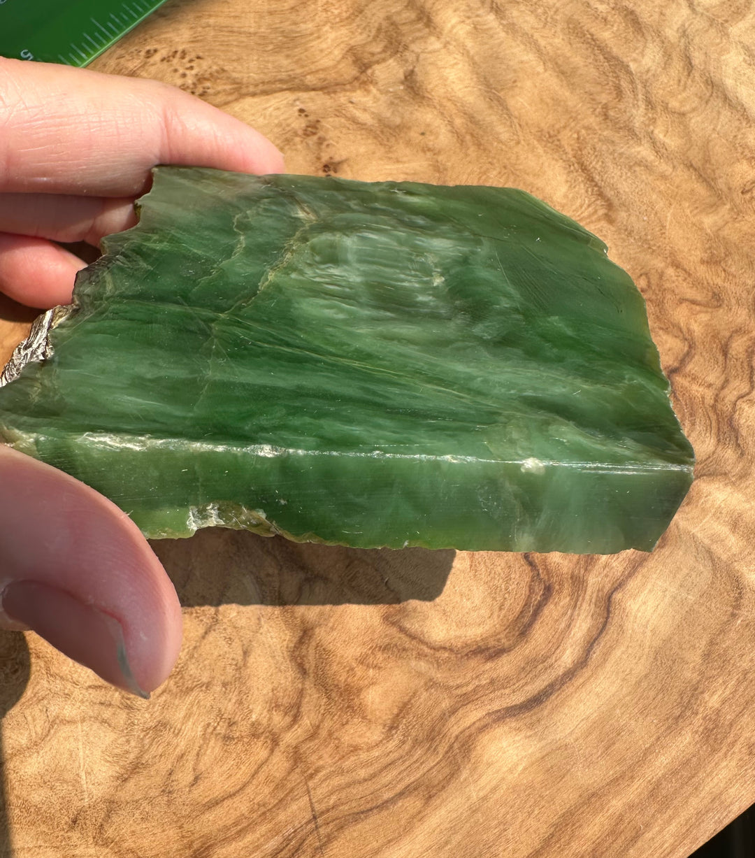 A hand holding a green jade with natural marbling, set against a wooden surface.
