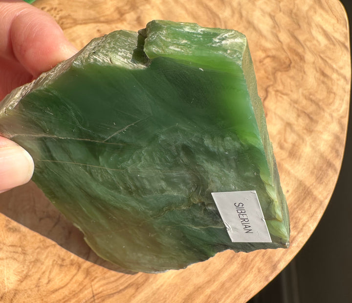 A hand holding a raw green stone slab labeled &