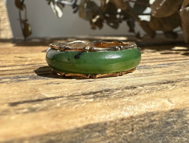 Vintage jade ring with a green stone set in a gold-toned bezel on a weathered wooden surface.