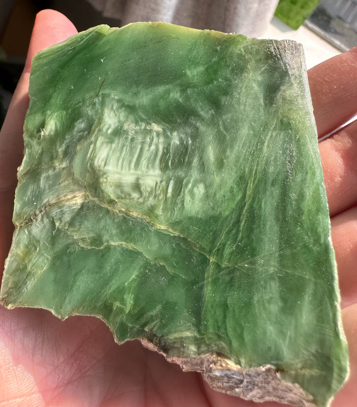 A raw green stone or mineral slab with natural striations and rough edges, held in a person&