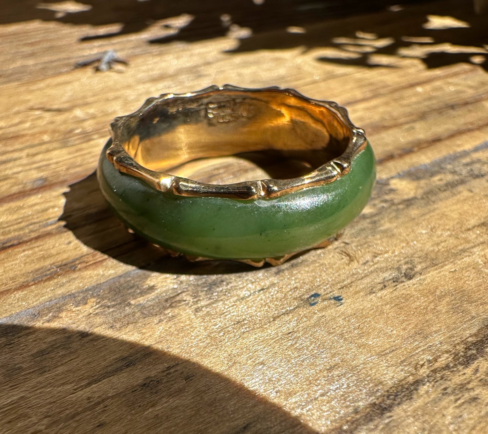 Vintage jade ring with a thick green jade band and gold setting on wood