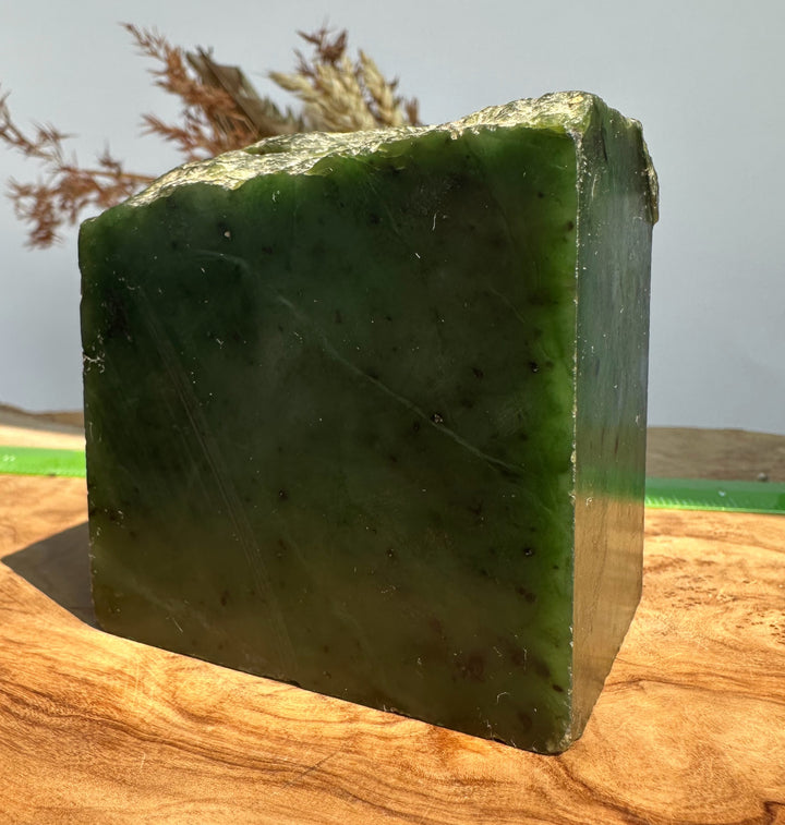 A rectangular green stone or polished slab with a rough natural top edge, standing on a wooden surface against a pale outdoor background.