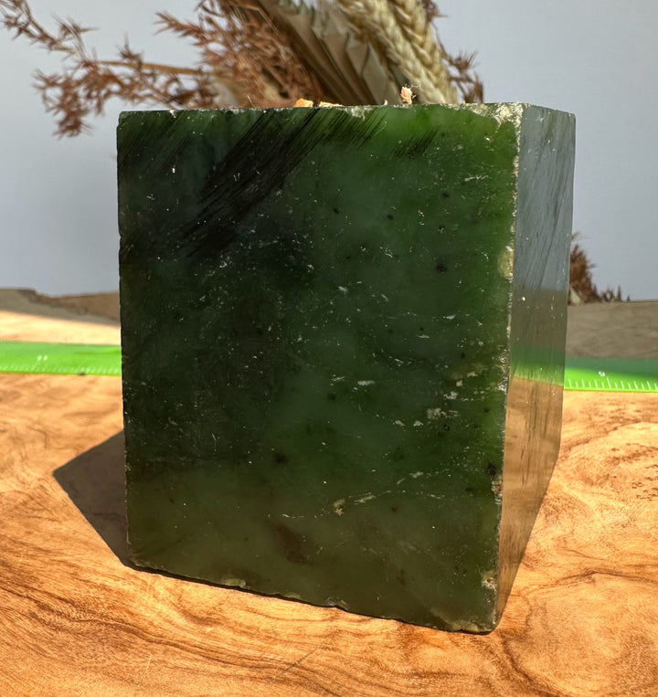 A rectangular green stone with a polished, slightly translucent surface, standing on a wooden surface with dried grass in the background.