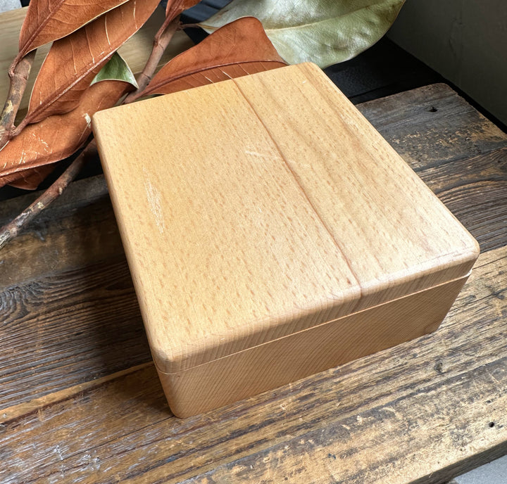 Light wood square jewelry box from Jade Wine Set on a rustic wooden table with dried leaves nearby.