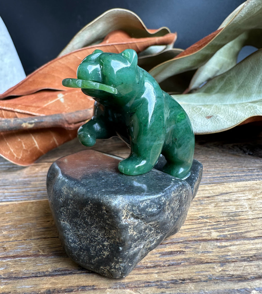 Side view of a green jade bear standing on a polished dark granite base.
