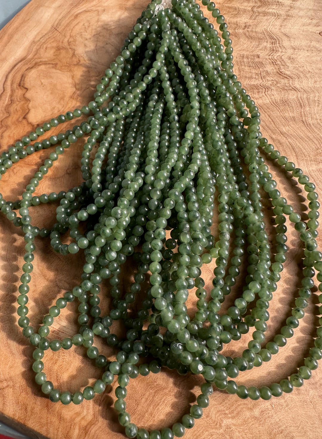 Numerous 4mm green nephrite jade beads arranged in strands on a wooden surface