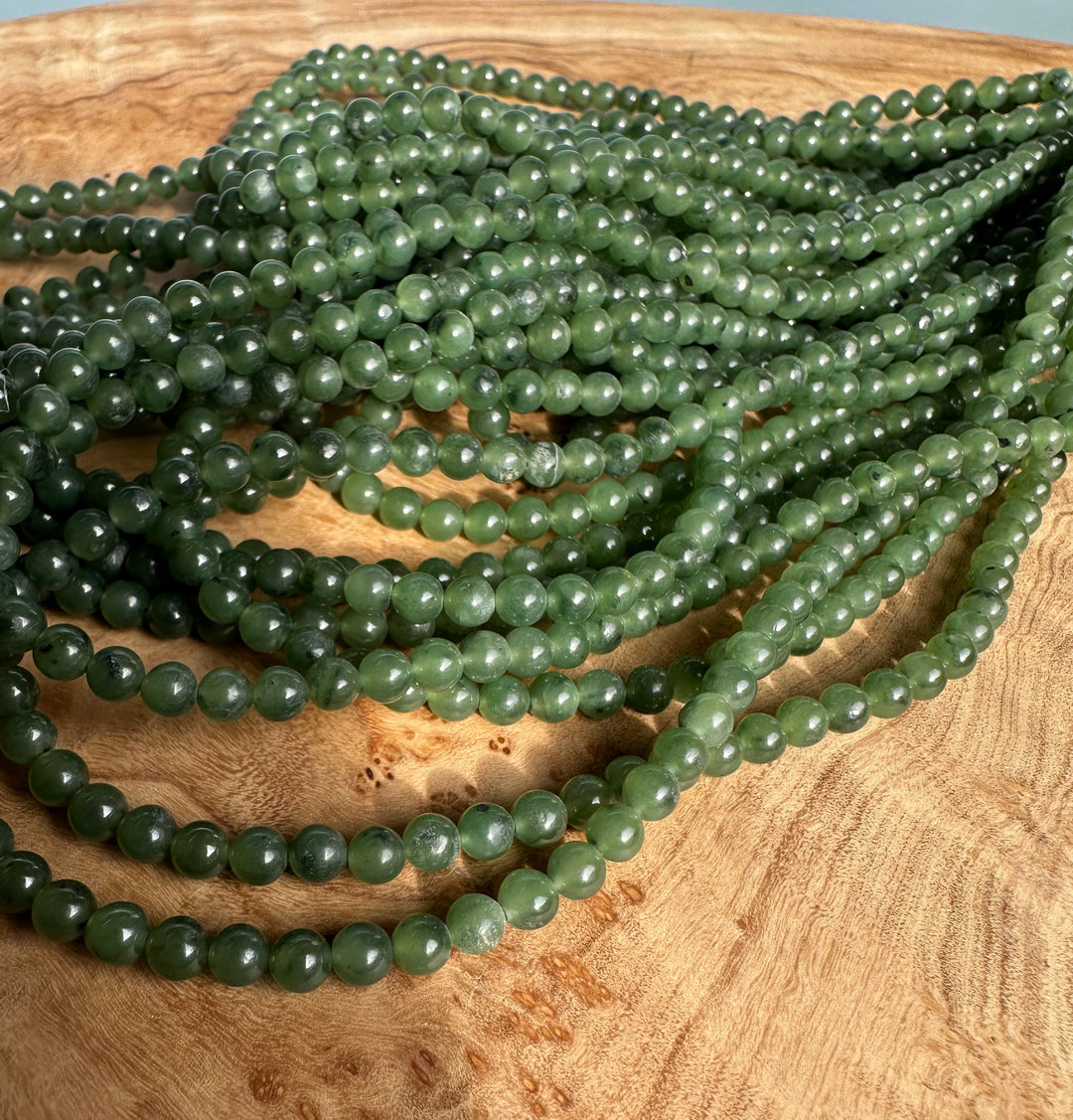 4mm nephrite jade beads on multiple unstrung strands resting on a wooden surface