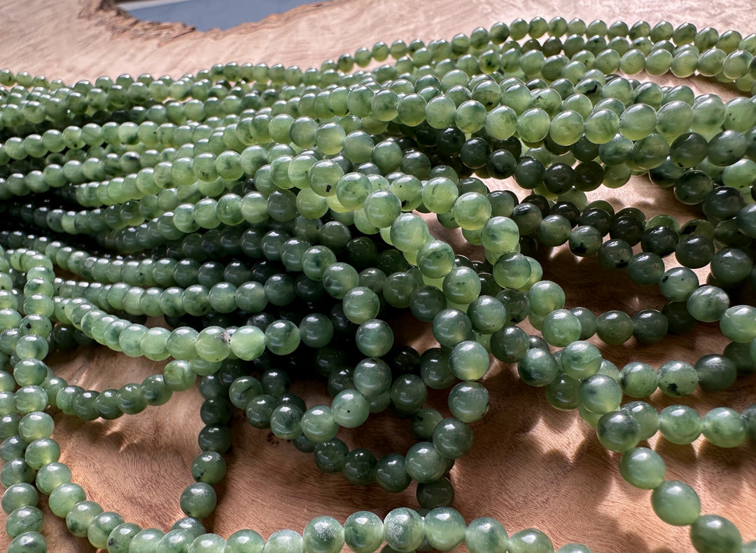 Multiple strands of 4mm nephrite jade beads piled on a wooden surface