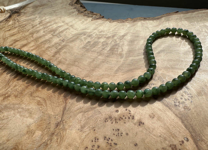 Unstrung 4mm nephrite jade beads in two strands on a wooden surface