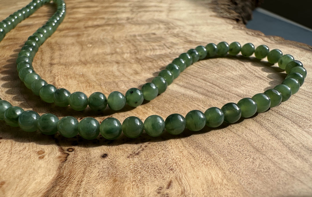 Curved strand of 4mm nephrite jade beads on a wooden surface