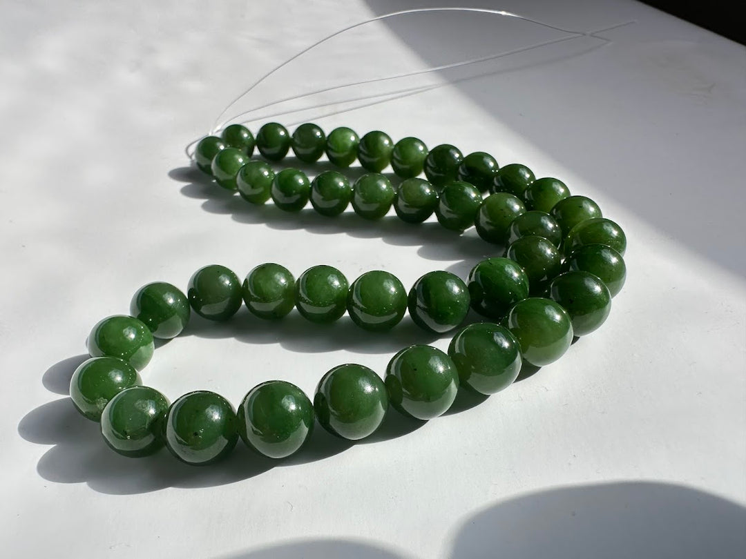 Unstrung glossy green 10mm beads laid in curved strands on a white surface.