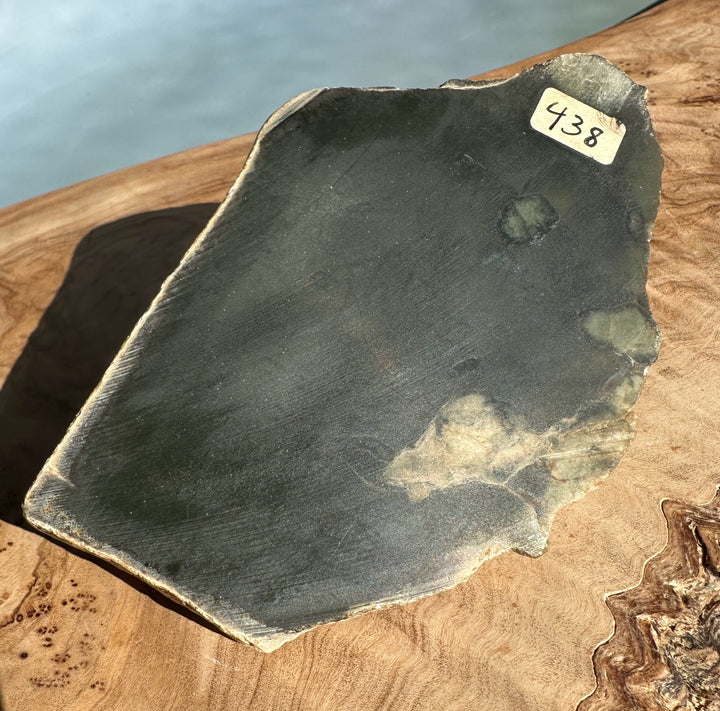 Dark slate slab with rough edges on a wooden surface and a sticker reading 438
