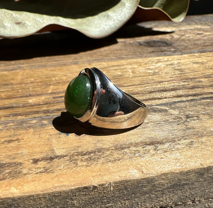 Side view of Canadian Jade Ring showing a green jade cabochon set in a thick silver band on wood.