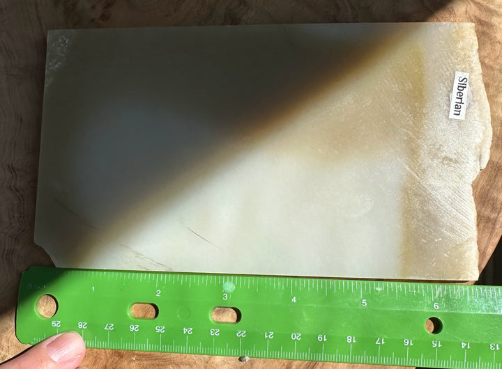 A jade slab of silver-gray stone, likely, shown with a green ruler for scale and a small &