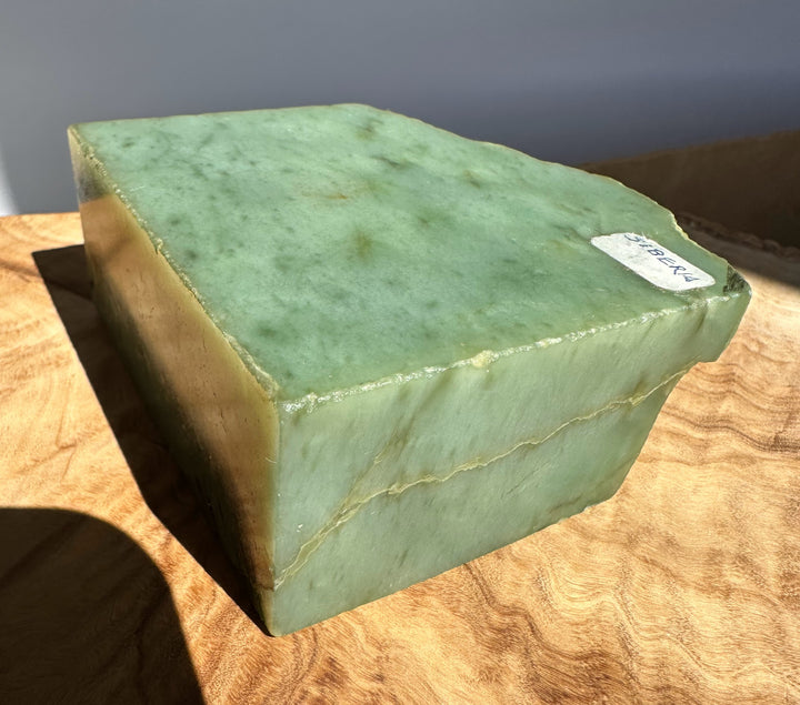 A green jade stone block with natural marbling and a small white label, displayed on a wooden surface.