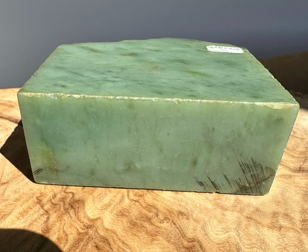 A rectangular block of light green jade stone with natural marbling, resting on a textured wooden surface.