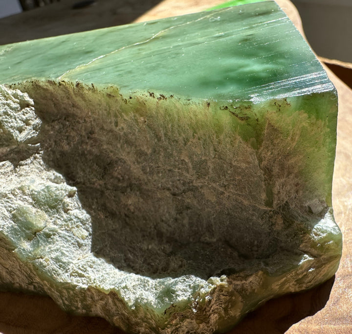 A green jade with a rough, textured light gray interior, photographed close-up on a wooden surface.