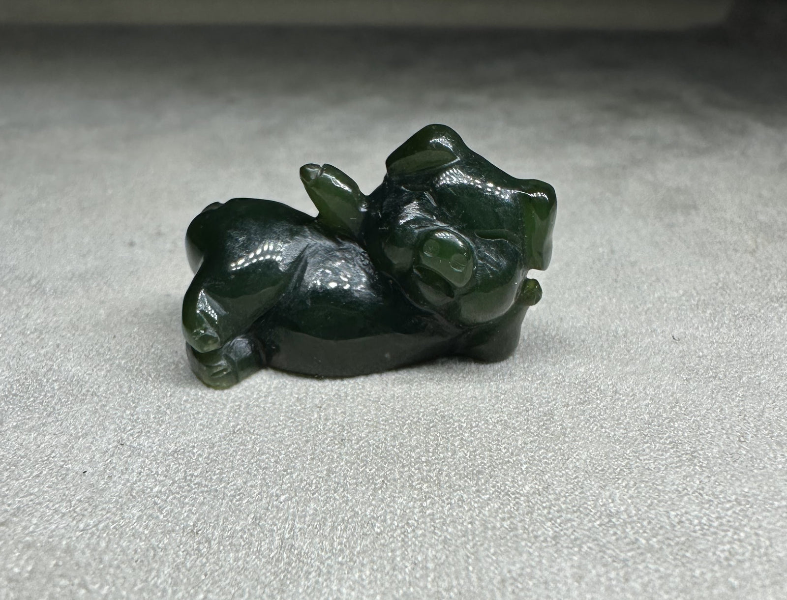 Dark green jade pig figurine lounging on its side
