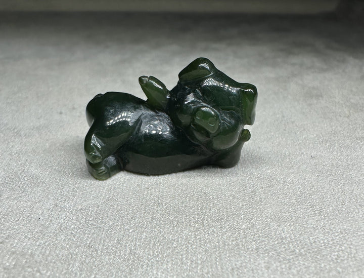 Dark green jade pig figurine lounging on its side