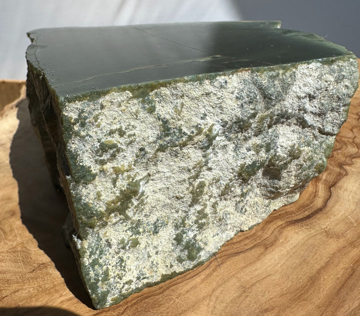 A natural stone slab with a smooth dark green top and a textured light green and white marbled side, displayed on a wooden surface.