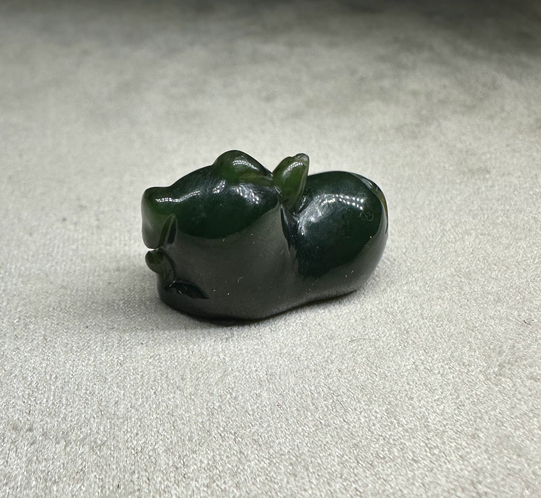Dark green glossy pig figurine lying on its side with a smooth rounded body