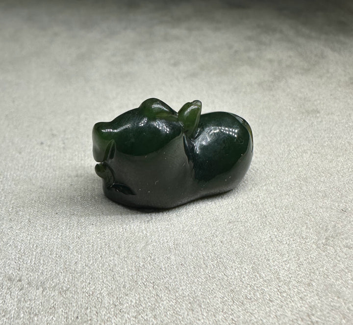 Dark green glossy pig figurine lying on its side with a smooth rounded body
