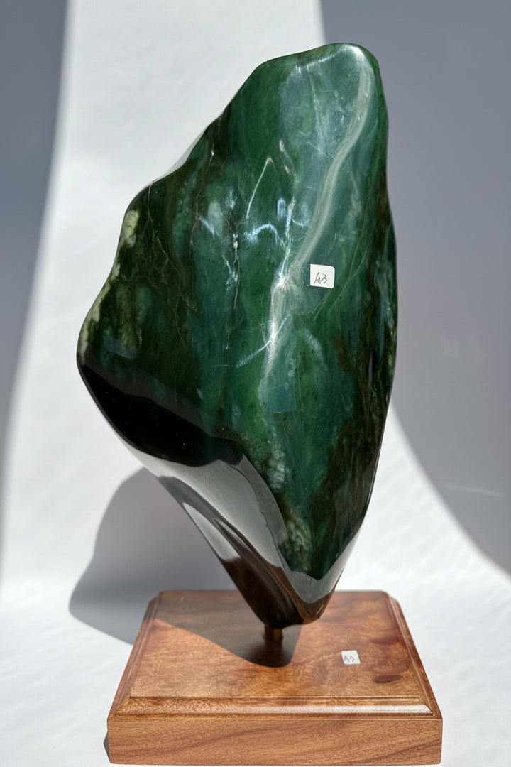 Polished Canadian Nephrite jade specimenon a wooden base with a white background