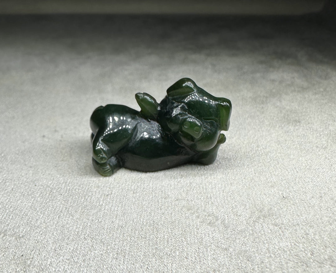Dark green glossy pig figurine resting on its side with head turned slightly to the side
