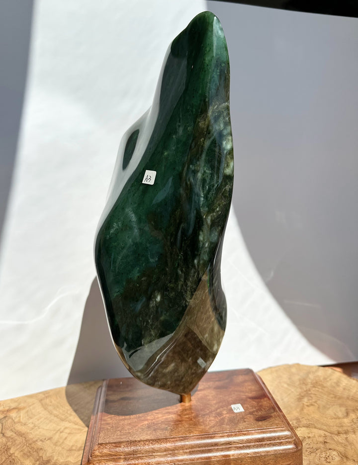 A polished dark green stone sculpture with natural marbling, displayed on a wooden stand against a white backdrop.