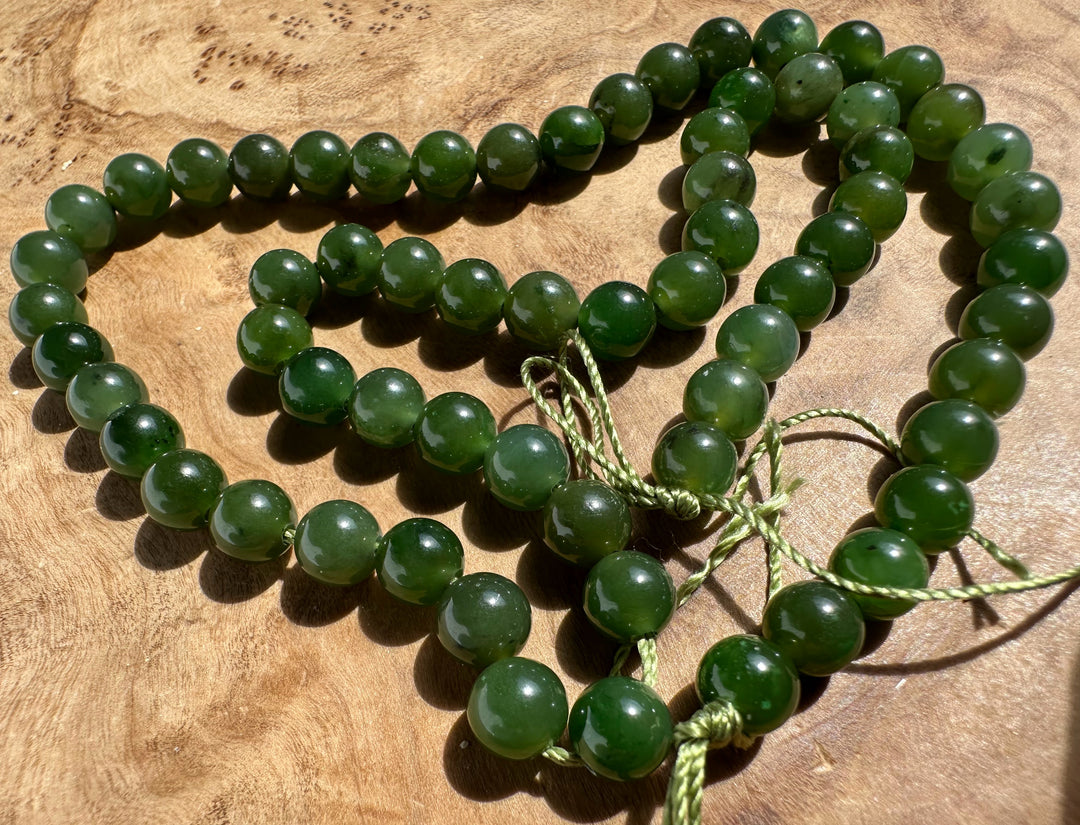 A strand of polished dark green jade beads with a matching green cord, arranged on a textured wooden surface.