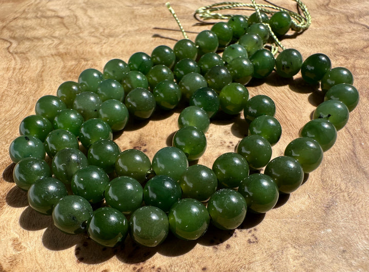 A strand of polished dark green jade beads arranged in a loop on a textured wooden surface, with a thin green cord visible at the top.