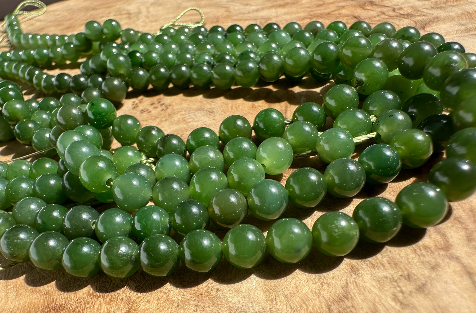Multiple strands of polished green gemstone beads arranged on a wooden surface.