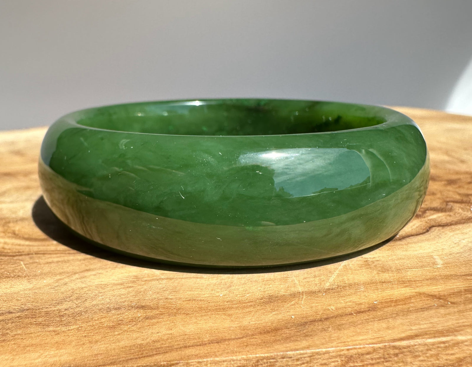 Close view of a polished A Grade Canadian Jade Bangle in green resting on a wooden surface.