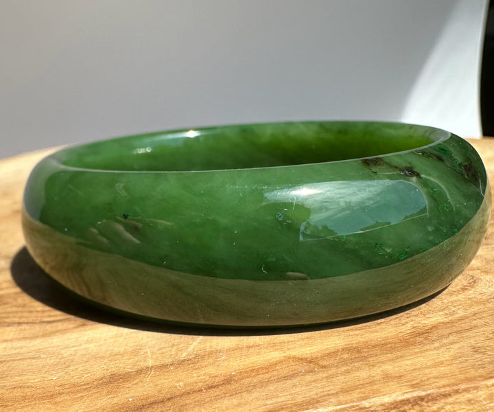 Polished emerald green jade bangle resting on a wooden surface 57.4 by 19.5 mm