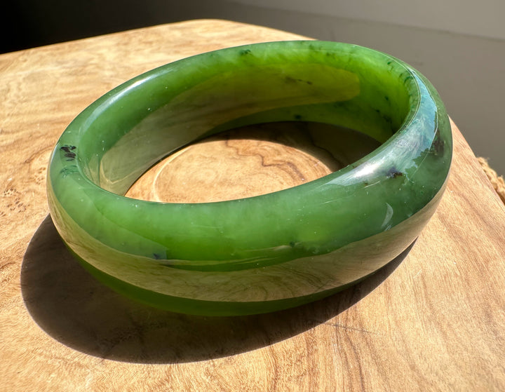 Side view of a green jade bangle resting on a wooden surface with a rounded, glossy exterior.